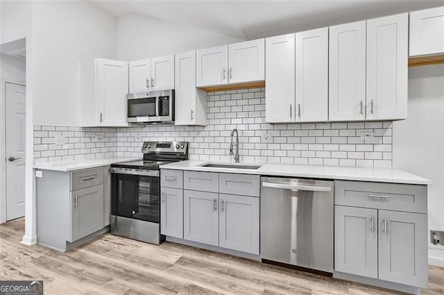 kitchen featuring sink, light hardwood / wood-style flooring, gray cabinets, appliances with stainless steel finishes, and tasteful backsplash