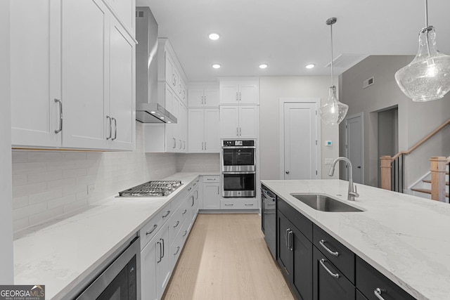 kitchen with sink, white cabinetry, appliances with stainless steel finishes, pendant lighting, and wall chimney range hood