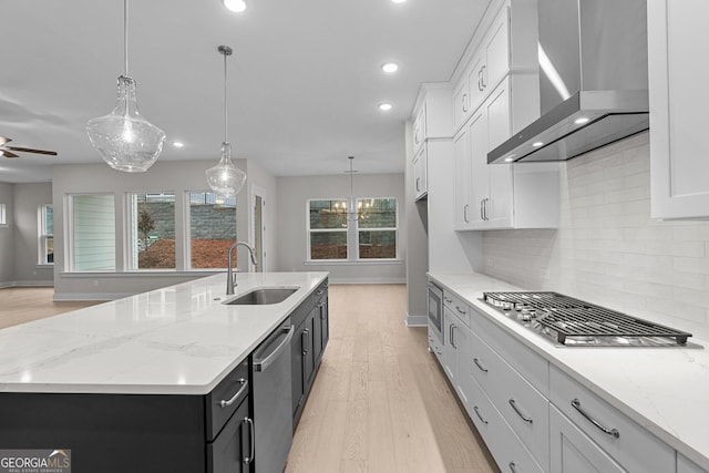 kitchen featuring wall chimney exhaust hood, decorative light fixtures, a kitchen island with sink, and white cabinets