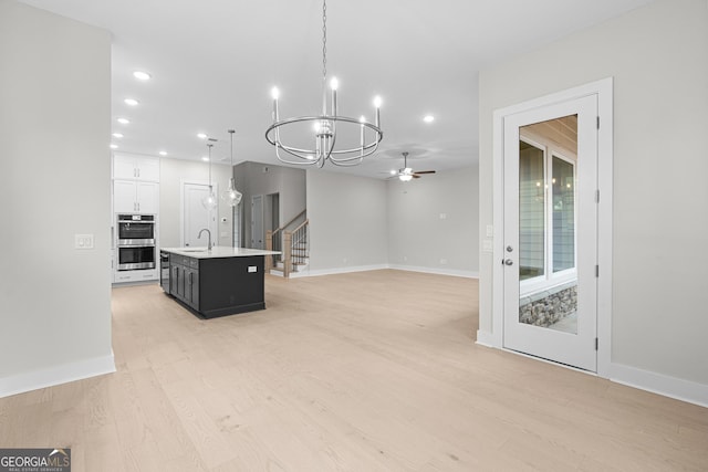 kitchen with sink, double oven, hanging light fixtures, an island with sink, and white cabinets