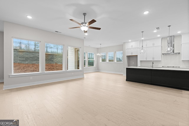 unfurnished living room featuring sink, ceiling fan with notable chandelier, and light hardwood / wood-style flooring