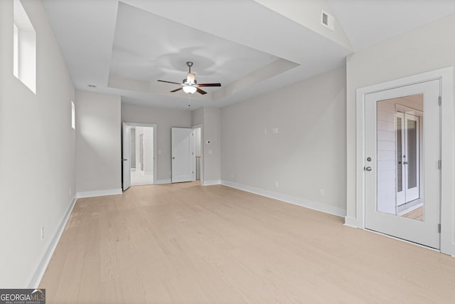 empty room with a raised ceiling, ceiling fan, and light wood-type flooring