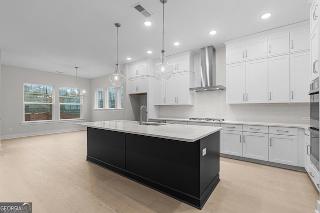 kitchen with pendant lighting, sink, white cabinets, a kitchen island with sink, and wall chimney exhaust hood