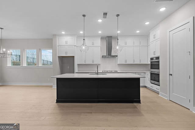 kitchen with pendant lighting, white cabinetry, wall chimney exhaust hood, and a kitchen island with sink