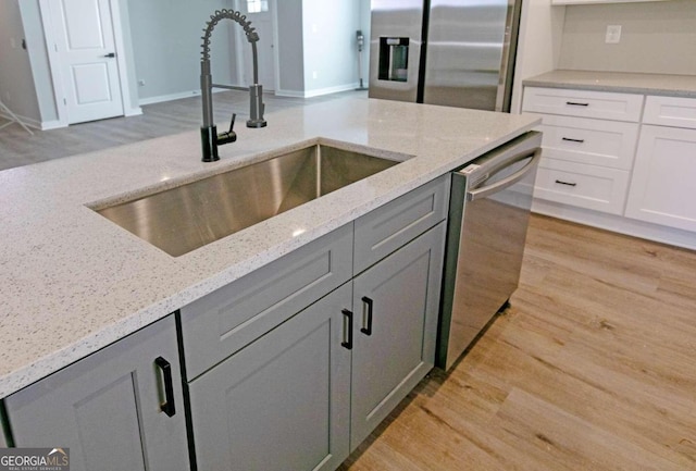 kitchen with sink, stainless steel appliances, light stone counters, gray cabinets, and light wood-type flooring