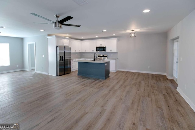 kitchen with white cabinets, stainless steel appliances, light hardwood / wood-style flooring, and an island with sink