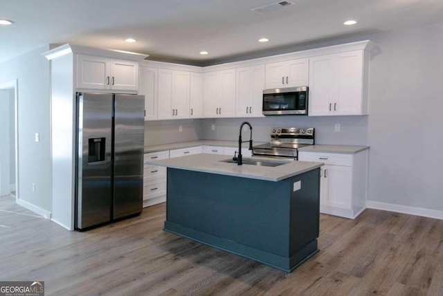 kitchen featuring white cabinetry, an island with sink, stainless steel appliances, and light wood-type flooring