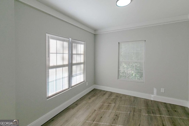 empty room with a healthy amount of sunlight, light wood-type flooring, and crown molding