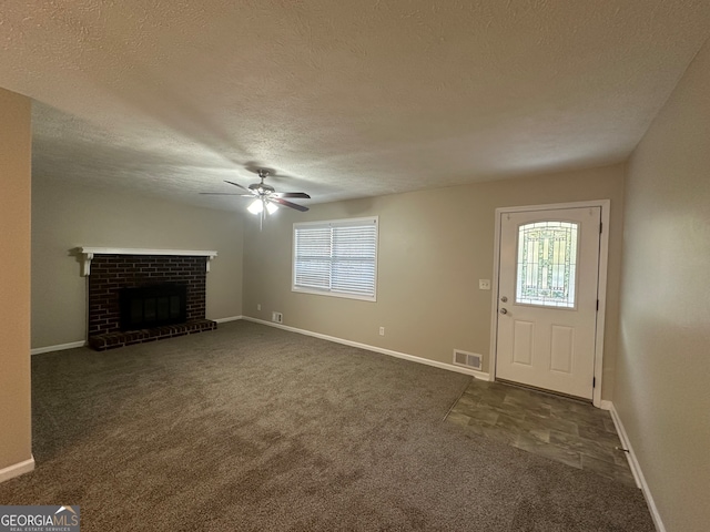 unfurnished living room featuring ceiling fan, dark carpet, a textured ceiling, and a brick fireplace