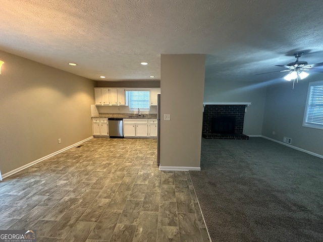 unfurnished living room with carpet flooring, ceiling fan, sink, a brick fireplace, and a textured ceiling