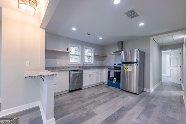 kitchen with white cabinets, wall chimney exhaust hood, light hardwood / wood-style floors, light stone counters, and stainless steel appliances