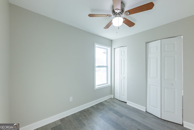 unfurnished bedroom featuring ceiling fan, light wood-type flooring, and two closets