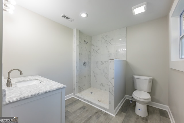 bathroom featuring vanity, toilet, a tile shower, and wood-type flooring