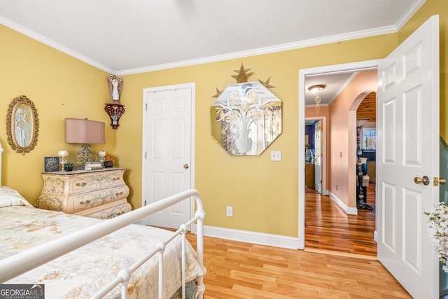 bedroom with crown molding, light wood-style floors, arched walkways, and baseboards