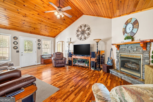 living room featuring a ceiling fan, wood finished floors, arched walkways, a stone fireplace, and wooden ceiling