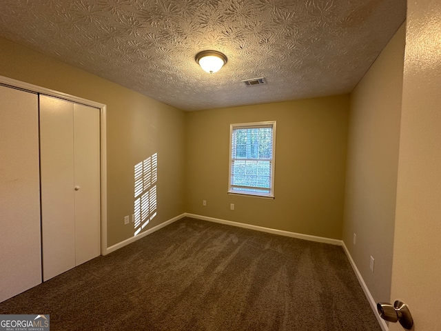 unfurnished bedroom with dark colored carpet, a textured ceiling, and a closet