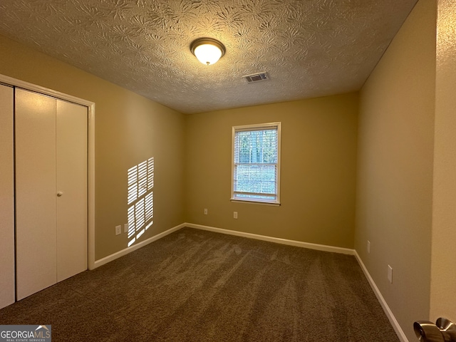 unfurnished bedroom featuring dark carpet, a textured ceiling, and a closet