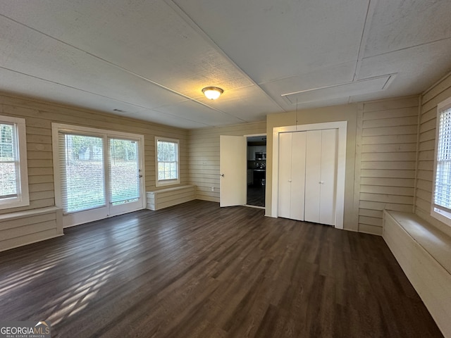 unfurnished bedroom with wood walls, dark wood-type flooring, and multiple windows