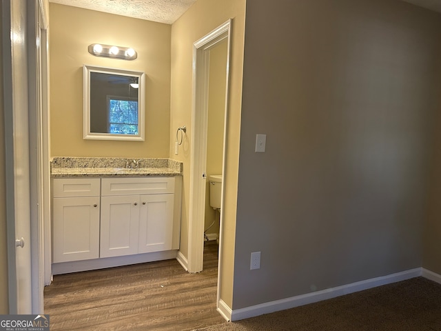 bathroom featuring vanity, a textured ceiling, hardwood / wood-style flooring, and toilet