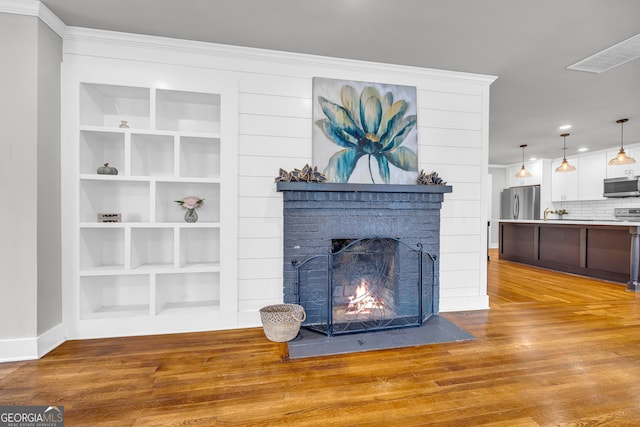 living room with built in shelves, a brick fireplace, crown molding, and wood-type flooring