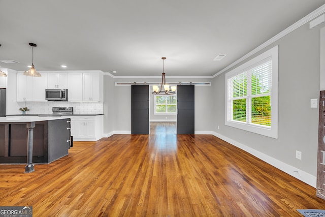 kitchen with pendant lighting, a barn door, white cabinetry, and appliances with stainless steel finishes