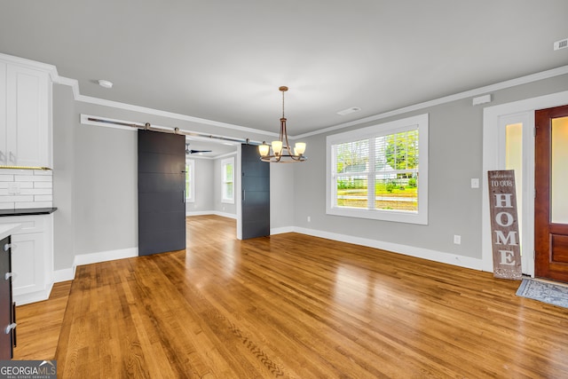 interior space with a barn door, an inviting chandelier, crown molding, and light hardwood / wood-style flooring