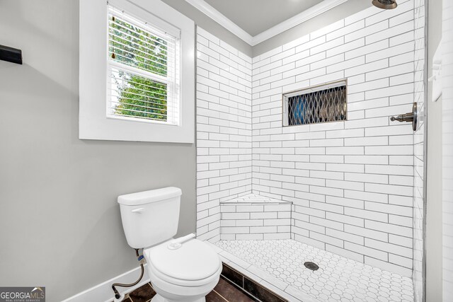 bathroom featuring a tile shower, toilet, and ornamental molding