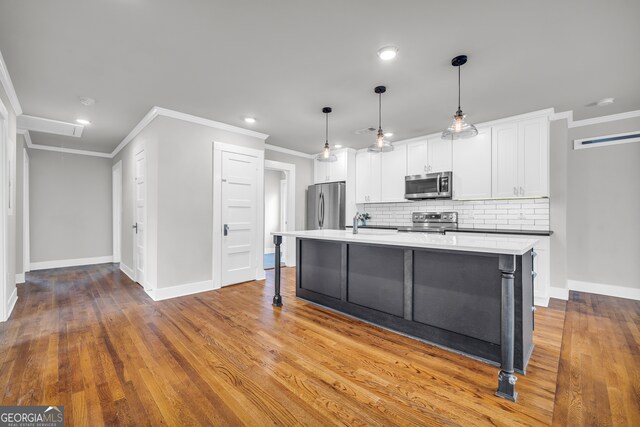 kitchen featuring pendant lighting, an island with sink, tasteful backsplash, white cabinetry, and stainless steel appliances