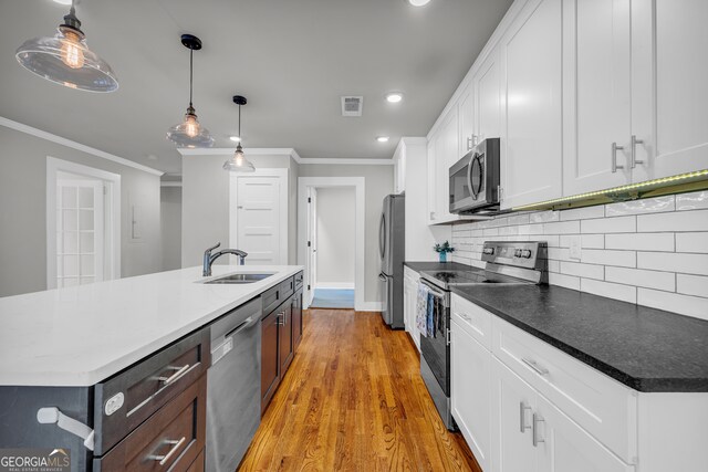 kitchen with appliances with stainless steel finishes, sink, decorative light fixtures, white cabinetry, and an island with sink