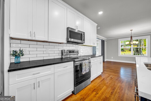 kitchen featuring dark stone counters, stainless steel appliances, crown molding, a barn door, and white cabinets