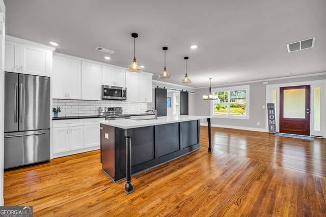 kitchen with a kitchen bar, stainless steel appliances, decorative light fixtures, a center island with sink, and white cabinets