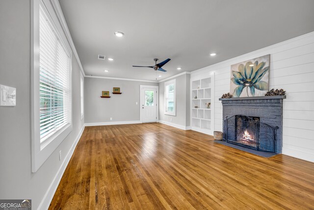 unfurnished living room featuring a brick fireplace, built in features, plenty of natural light, and crown molding