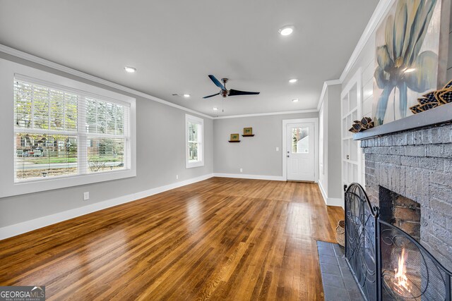 unfurnished living room featuring hardwood / wood-style flooring, ceiling fan, crown molding, and a brick fireplace