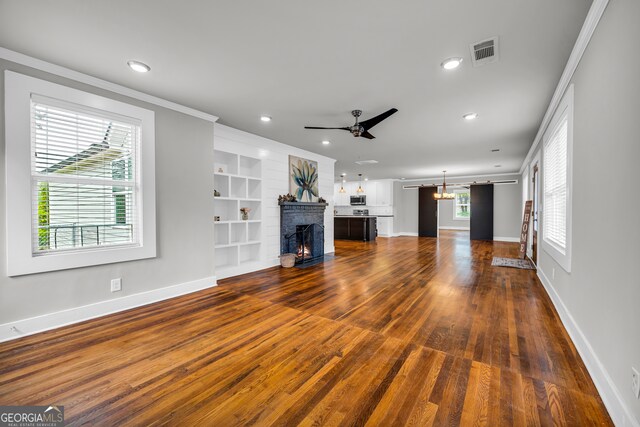 unfurnished living room featuring built in shelves, ornamental molding, ceiling fan, and dark wood-type flooring