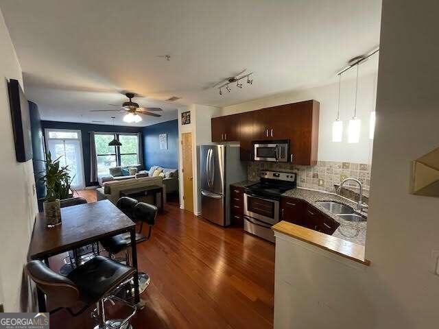 kitchen with decorative backsplash, appliances with stainless steel finishes, dark brown cabinets, sink, and dark hardwood / wood-style floors