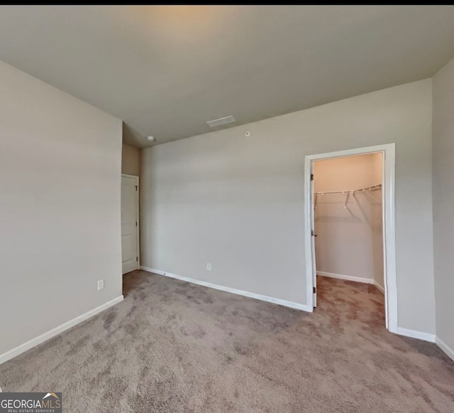 unfurnished bedroom with a spacious closet, light carpet, and a closet