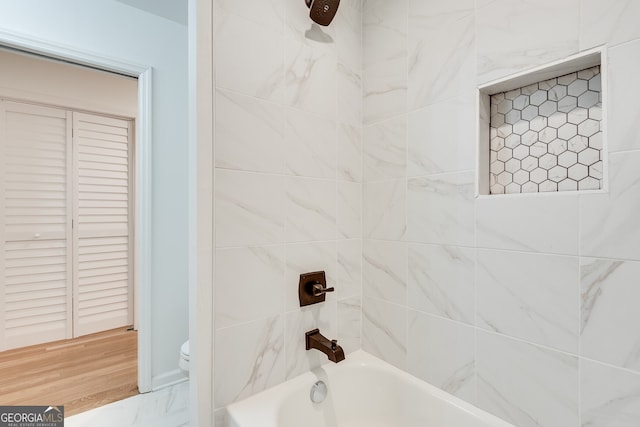 bathroom featuring tiled shower / bath combo, hardwood / wood-style flooring, and toilet