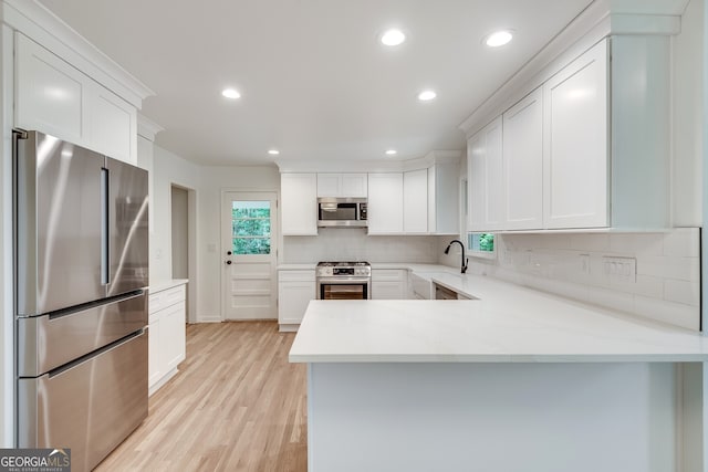 kitchen with backsplash, white cabinets, light hardwood / wood-style flooring, appliances with stainless steel finishes, and kitchen peninsula