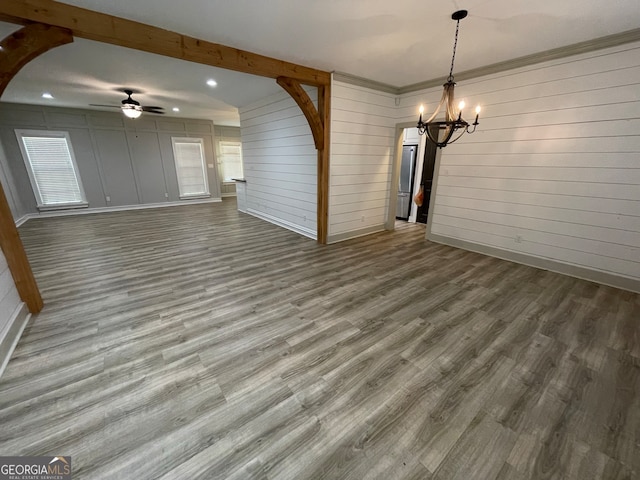 unfurnished dining area with wood walls, ceiling fan with notable chandelier, hardwood / wood-style flooring, ornamental molding, and beam ceiling