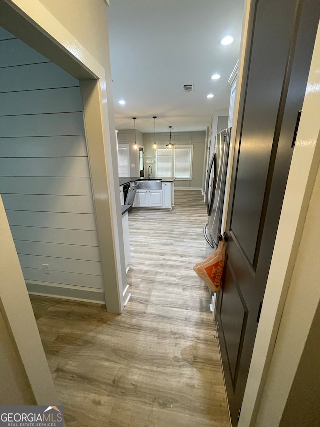 kitchen featuring light wood-type flooring, sink, white cabinets, stainless steel refrigerator, and hanging light fixtures