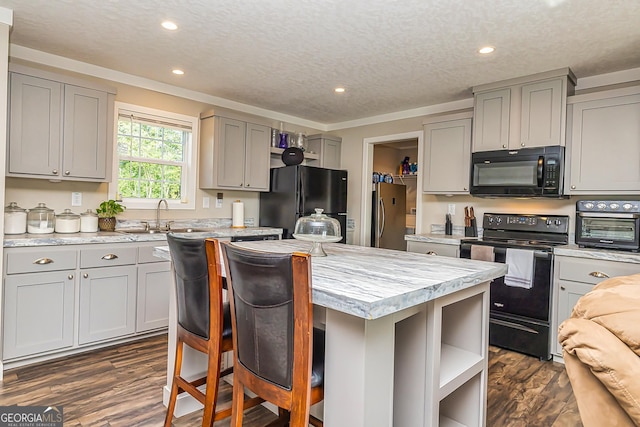 kitchen with a kitchen breakfast bar, ornamental molding, a textured ceiling, black appliances, and a center island