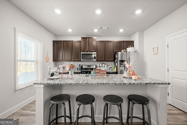 kitchen featuring light hardwood / wood-style floors, appliances with stainless steel finishes, a breakfast bar, and an island with sink