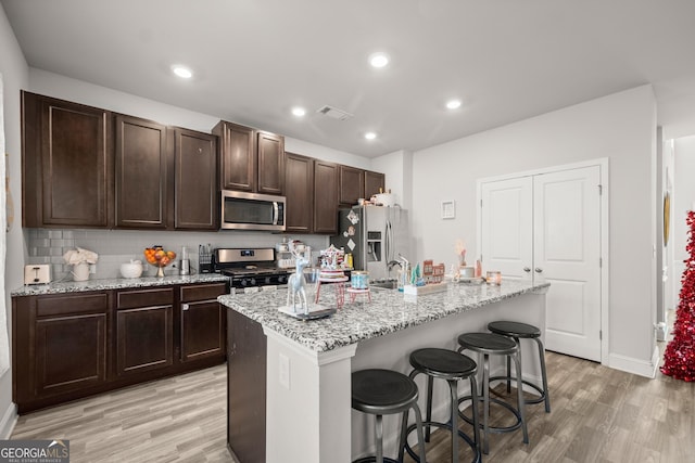 kitchen featuring a kitchen bar, light stone counters, light wood-type flooring, stainless steel appliances, and a kitchen island with sink