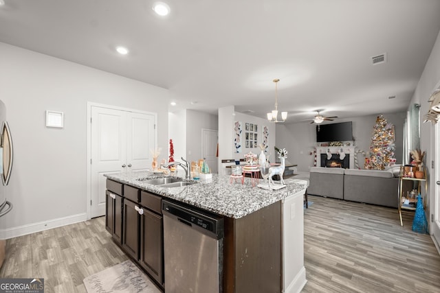 kitchen with sink, appliances with stainless steel finishes, a kitchen island with sink, dark brown cabinets, and light stone counters