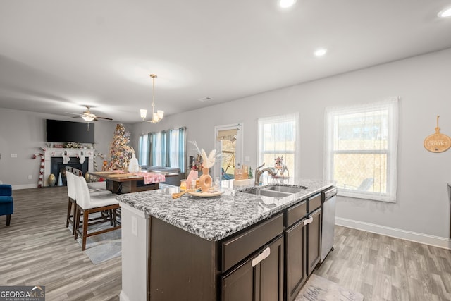 kitchen featuring sink, dark brown cabinets, hanging light fixtures, dishwasher, and a kitchen island with sink