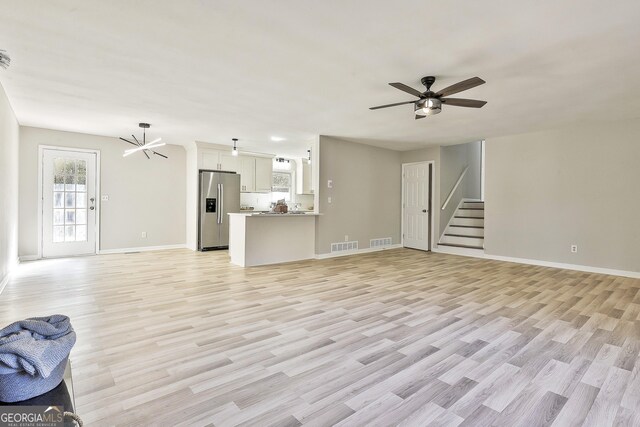 unfurnished living room featuring ceiling fan with notable chandelier and light hardwood / wood-style flooring