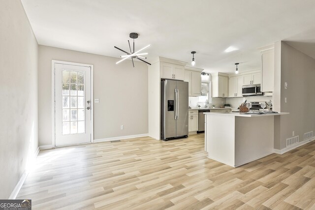 kitchen with white cabinetry, hanging light fixtures, stainless steel appliances, kitchen peninsula, and light hardwood / wood-style floors