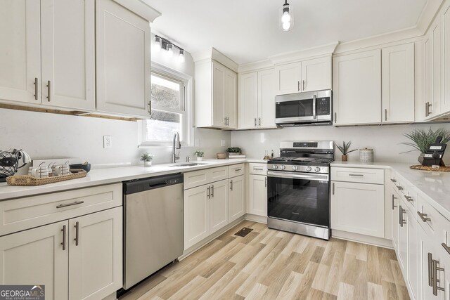 kitchen featuring sink, white cabinets, stainless steel appliances, and light hardwood / wood-style flooring