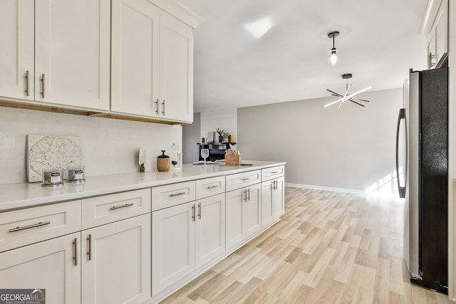 kitchen with white cabinets, decorative light fixtures, stainless steel fridge, and light hardwood / wood-style floors