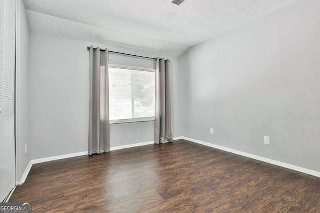 empty room with a textured ceiling, vaulted ceiling, and dark wood-type flooring